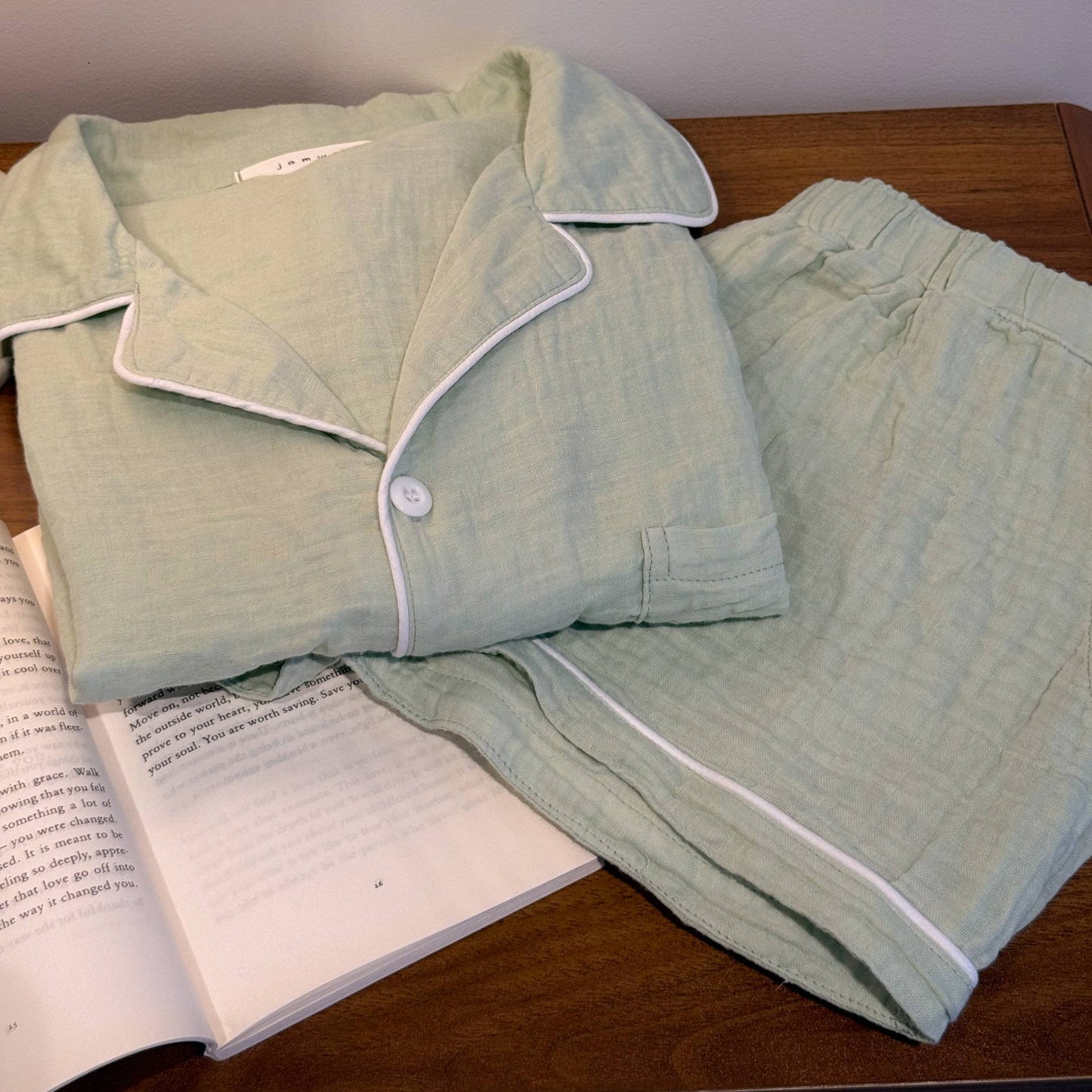 Sage green pajama set on a wooden surface with an open book underneath