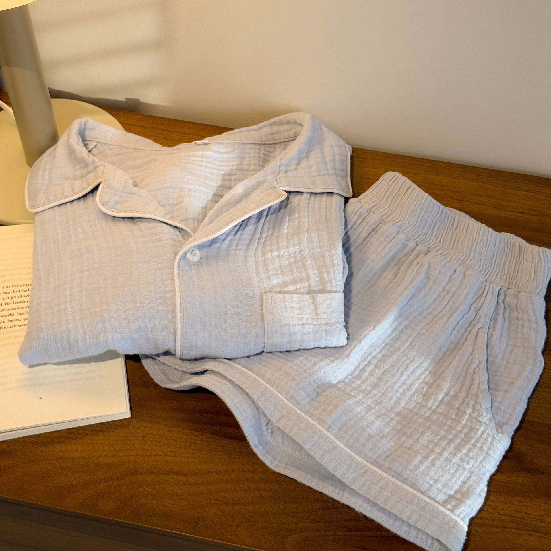 Folded dusty blue shirt and shorts on a wooden surface with a lamp in the background.